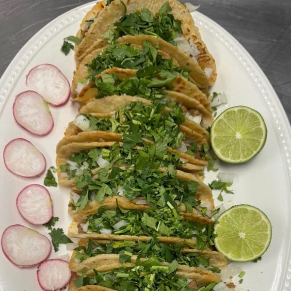 A white platter filled with Mi Rinconcito's Mexican tacos, garnished with cilantro, onions, radishes, and lime.