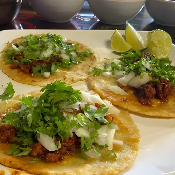 Three Mi Rinconcito tacos with meat, cilantro, and onions, served with lime wedges.